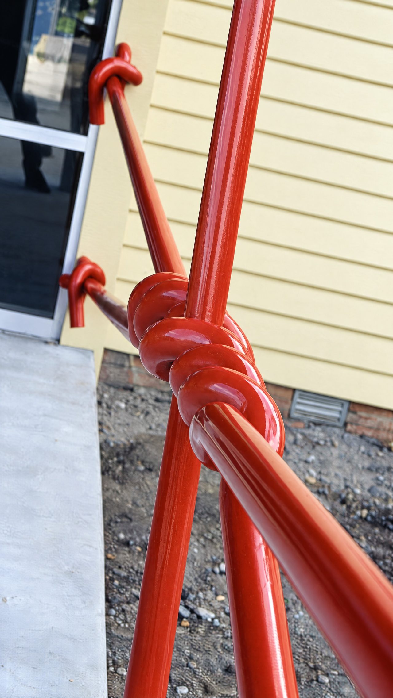Strainer, a close view of knotted red steel rods against yellow weatherboard cladding at Spreyton Primary School, by David Hamilton