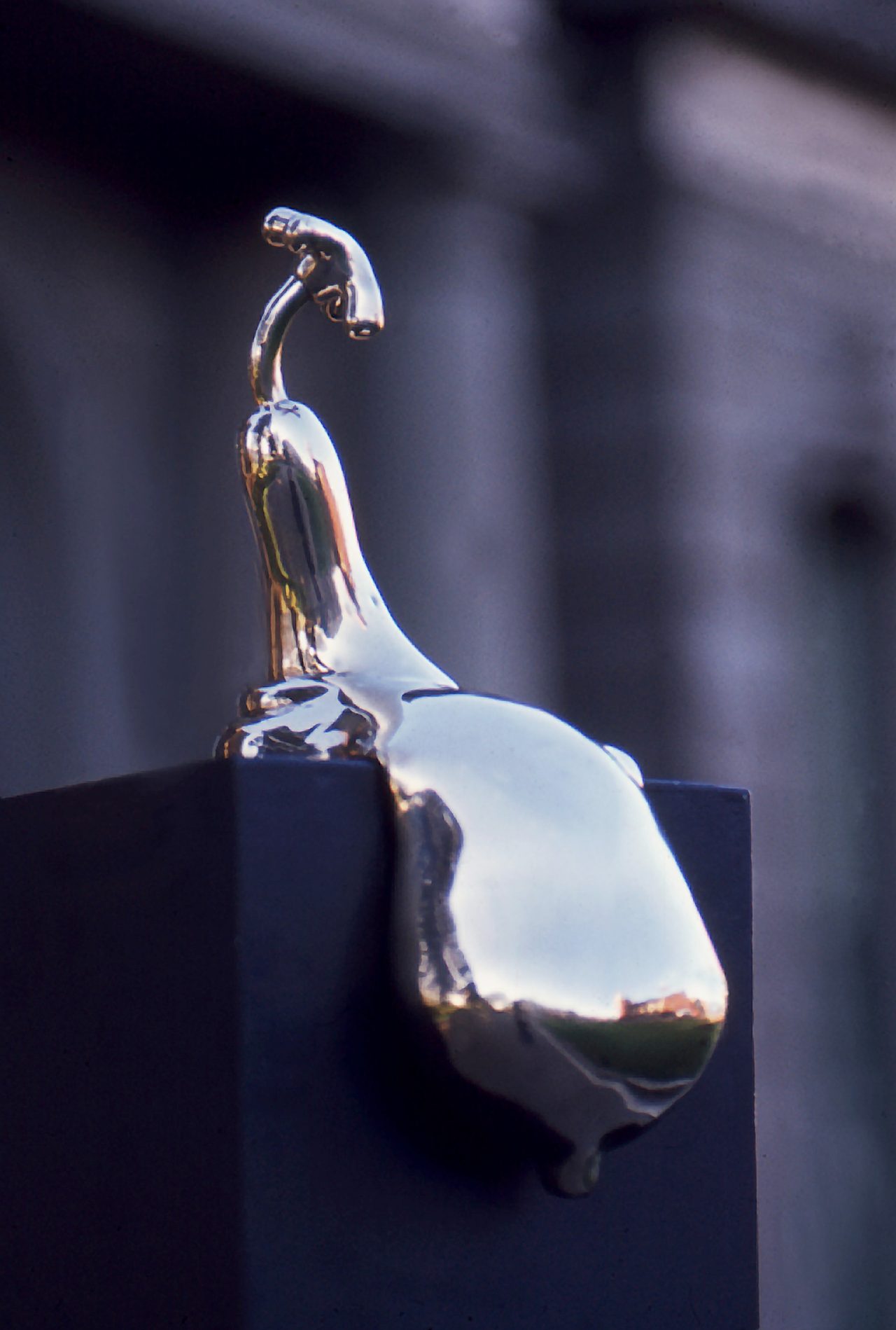 Hot, a polished bronze bird-like curved neck topped by a cross-handled tap, mounted on a dark plinth, by David Hamilton