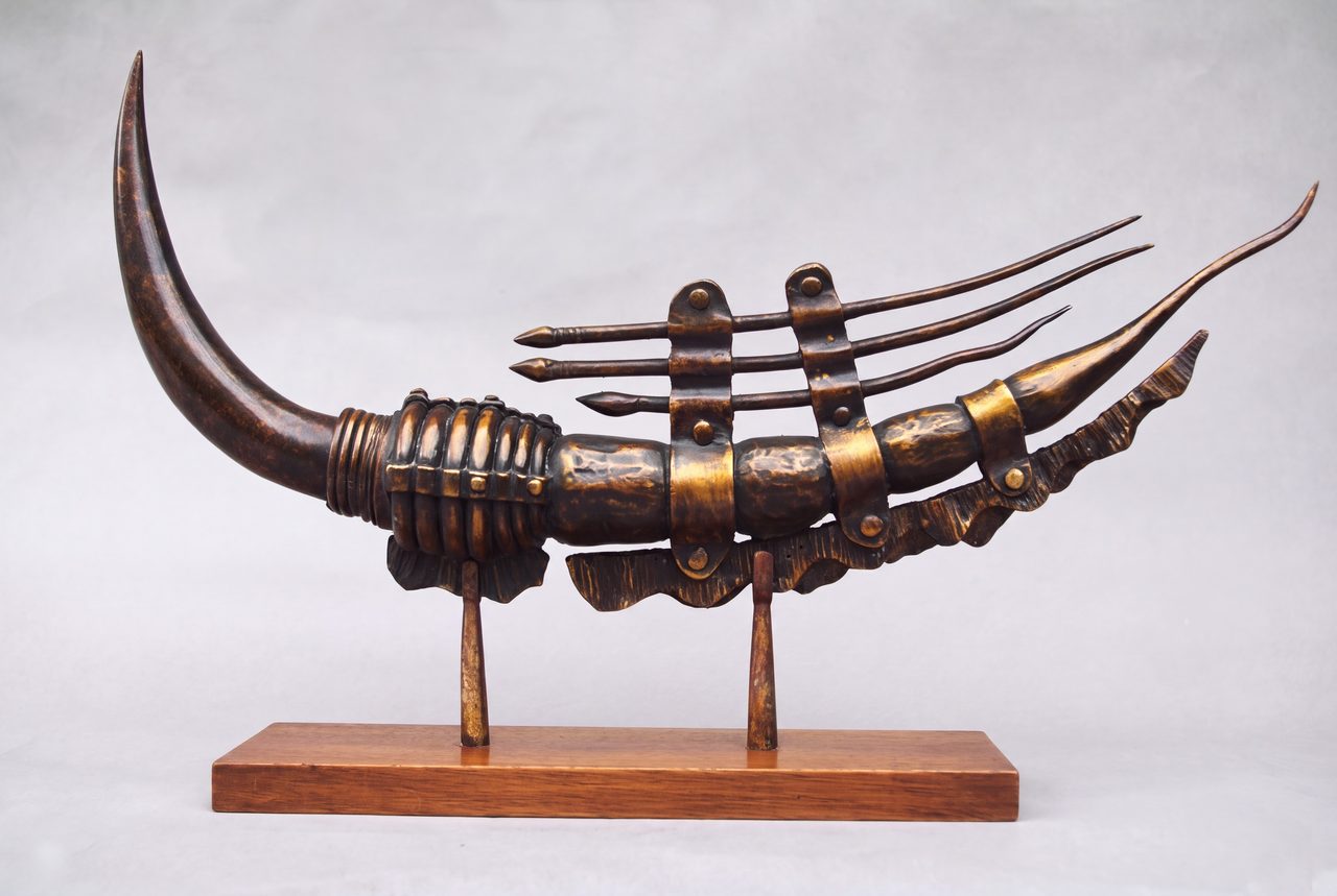 Razor, a curved bronze horn banded with rivets and rings, sprouting several thin curved spikes, raised on two stands, by David Hamilton