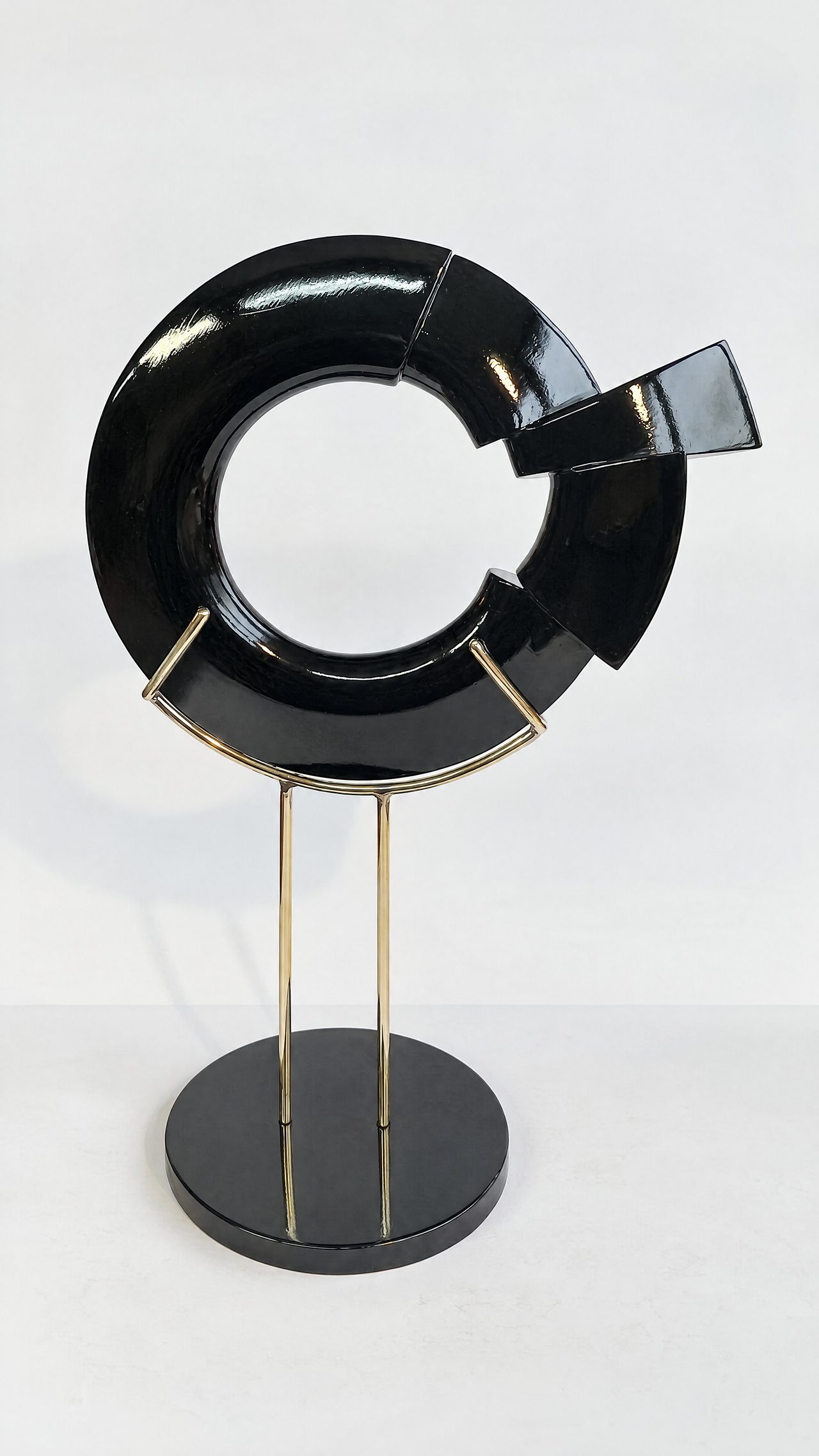A broken-ring sculpture in glossy black lacquer with a twisted knot at its base, mounted on a stand, by David Hamilton