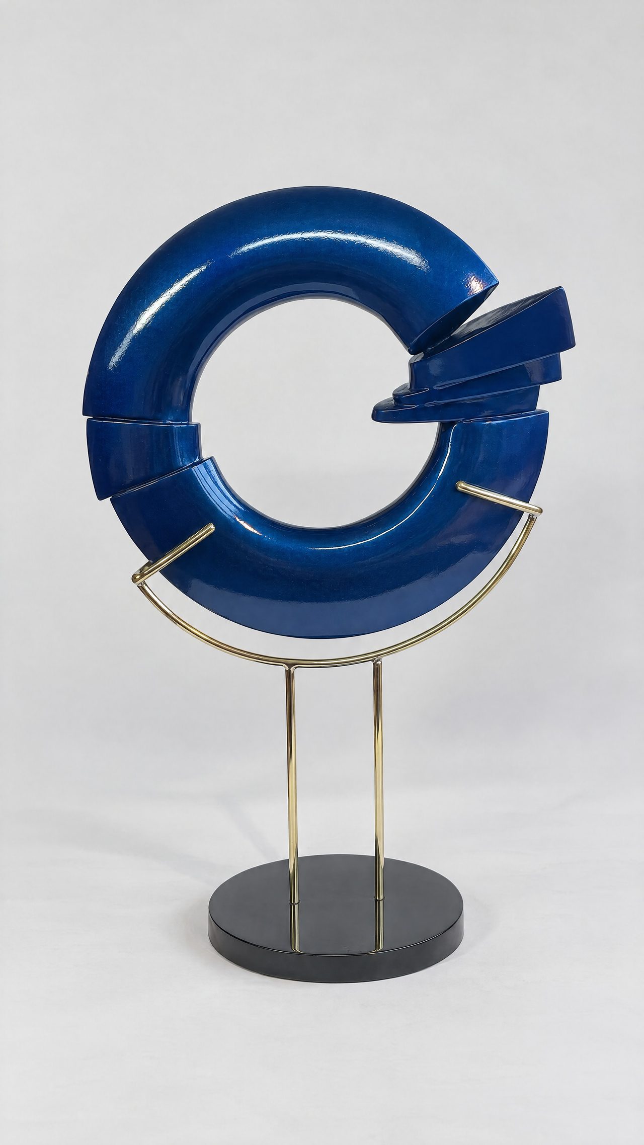 A broken-ring sculpture in metallic blue-grey lacquer with a twisted knot at its base, mounted on a stand, by David Hamilton