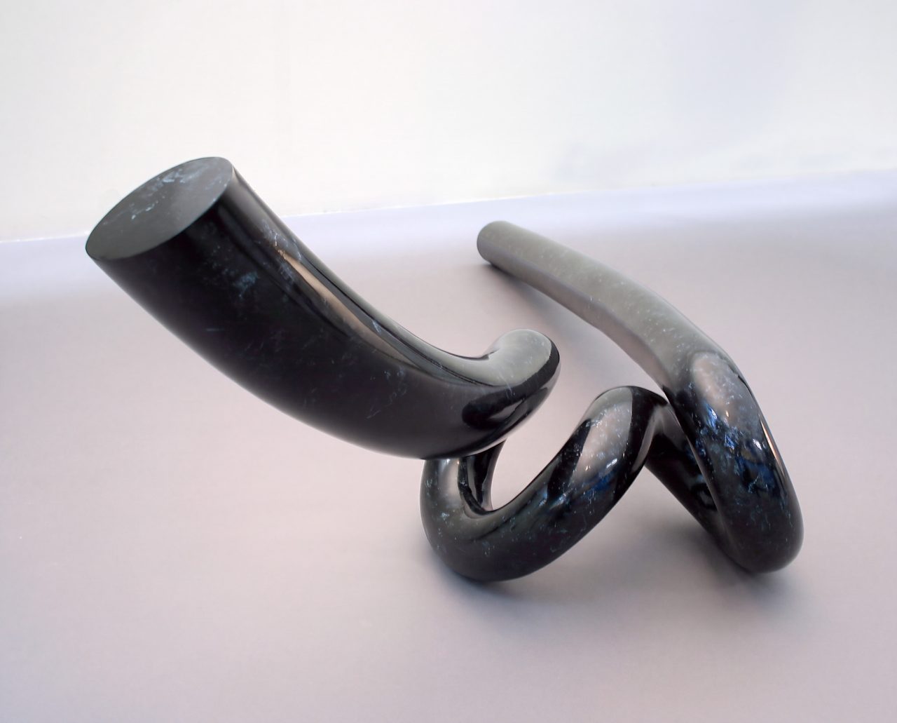 Thread, two dark curved steel rods, one with a coiled loop, leaning together on a pale surface, by David Hamilton