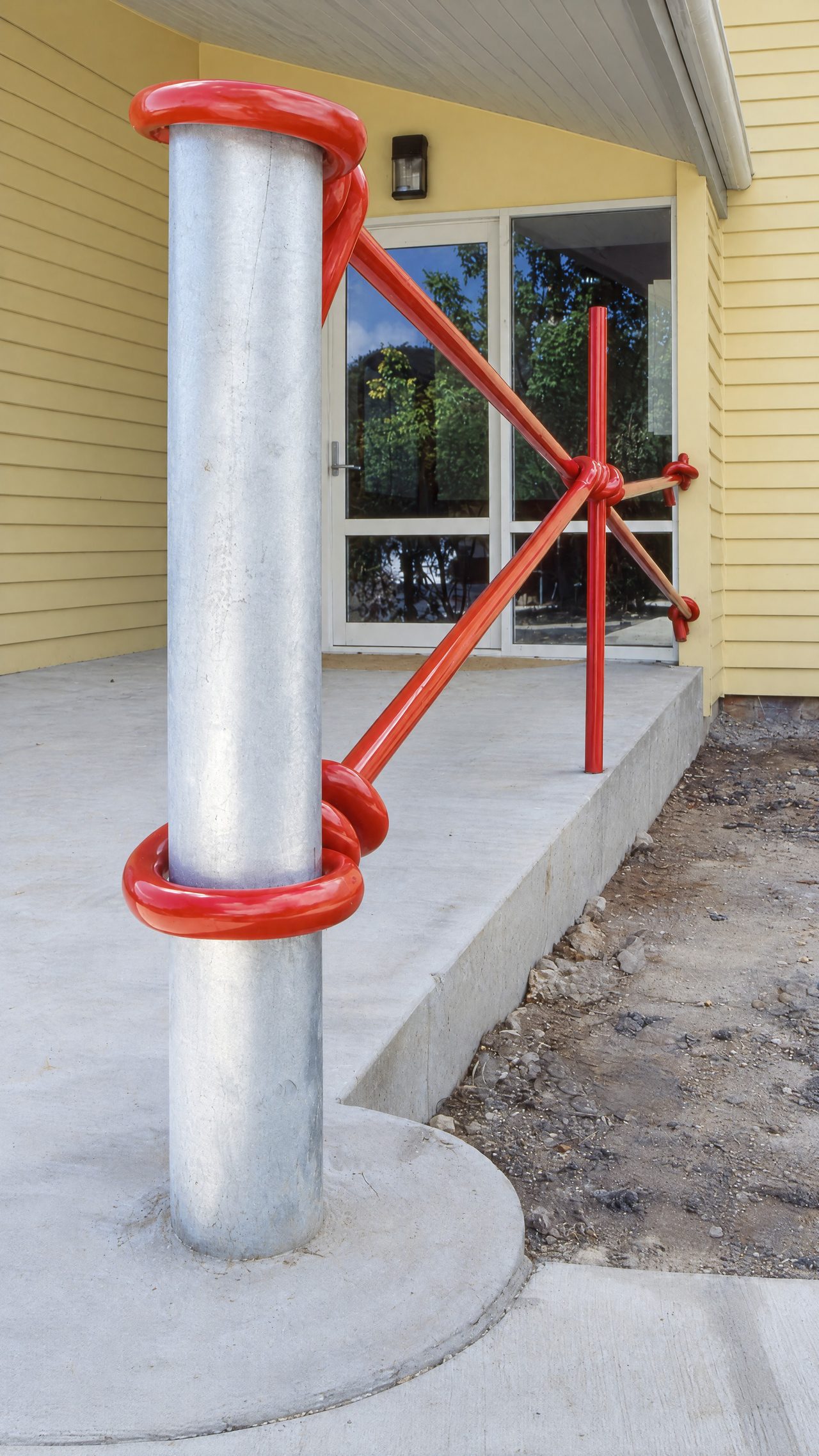 Strainer, a red painted steel handrail knotted around a fence post outside Spreyton Primary School, by David Hamilton