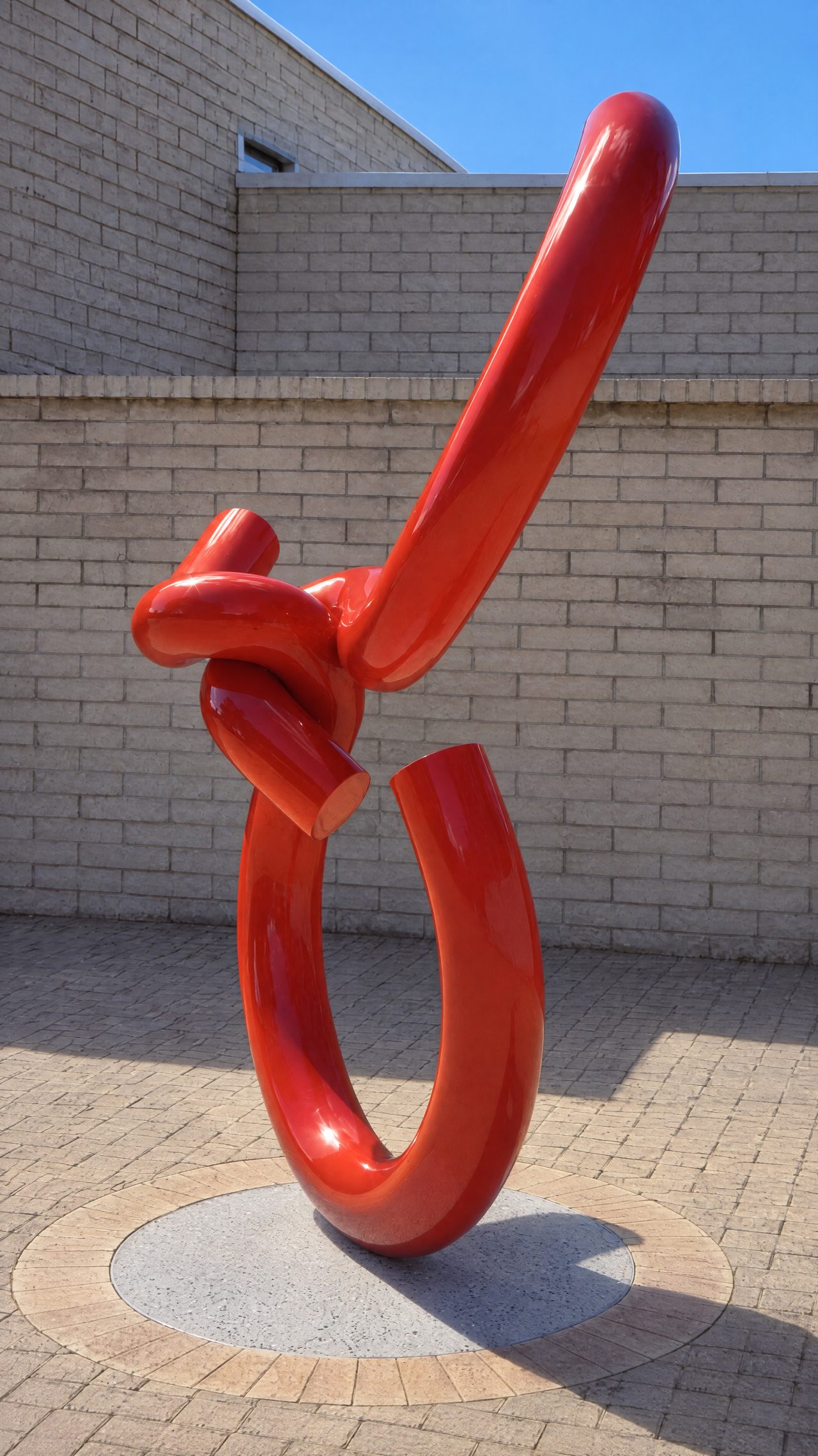 Y2, a red painted steel sculpture of knotted, looping rods standing against a brick wall on the UTAS Newnham campus, by David Hamilton