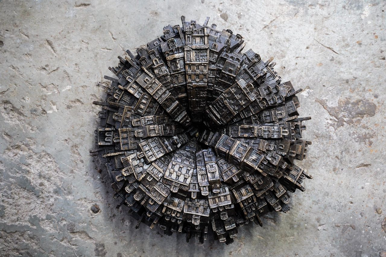City Depths, a silicon bronze ring of tiny buildings spiralling inward around a dark centre, seen from above on concrete, by David Hamilton