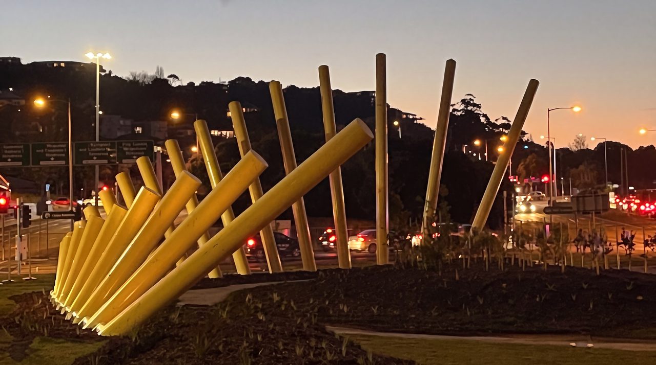 Welcome Gesture at dusk: leaning yellow poles lit from below at the Burnie roadside