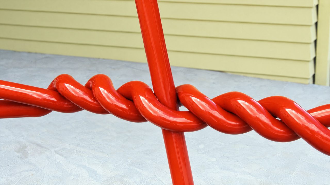 Strainer, a close view of a twisted red steel rod knot crossing a straight upright rod at Spreyton Primary School, by David Hamilton