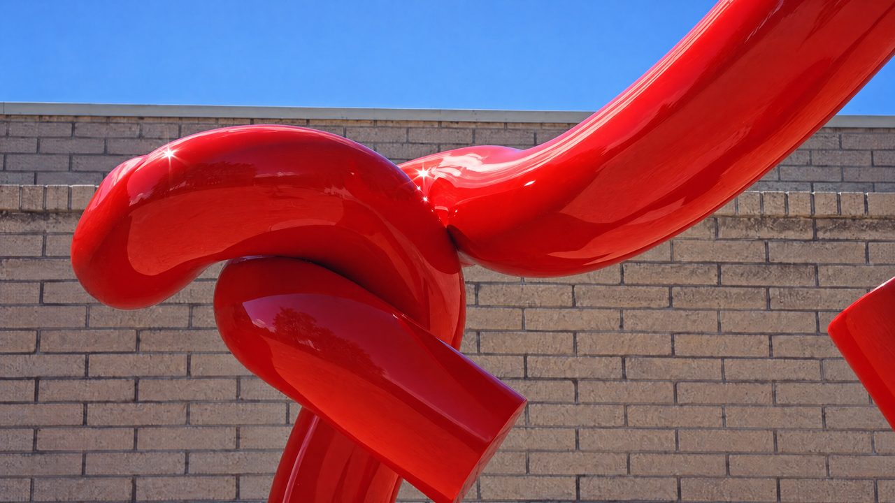 Y2, a close view of the tight knotted joint at the centre of a red painted steel rod sculpture, by David Hamilton