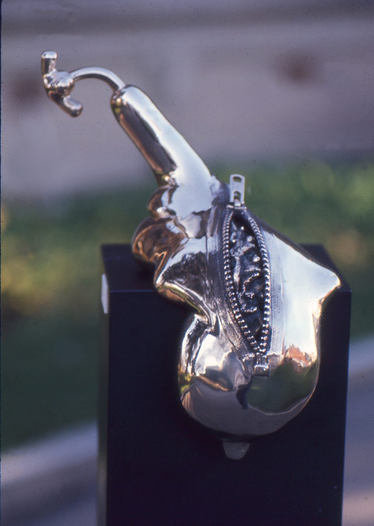 Zip, a polished bronze rounded form with a zip fastener embossed down one side, by David Hamilton