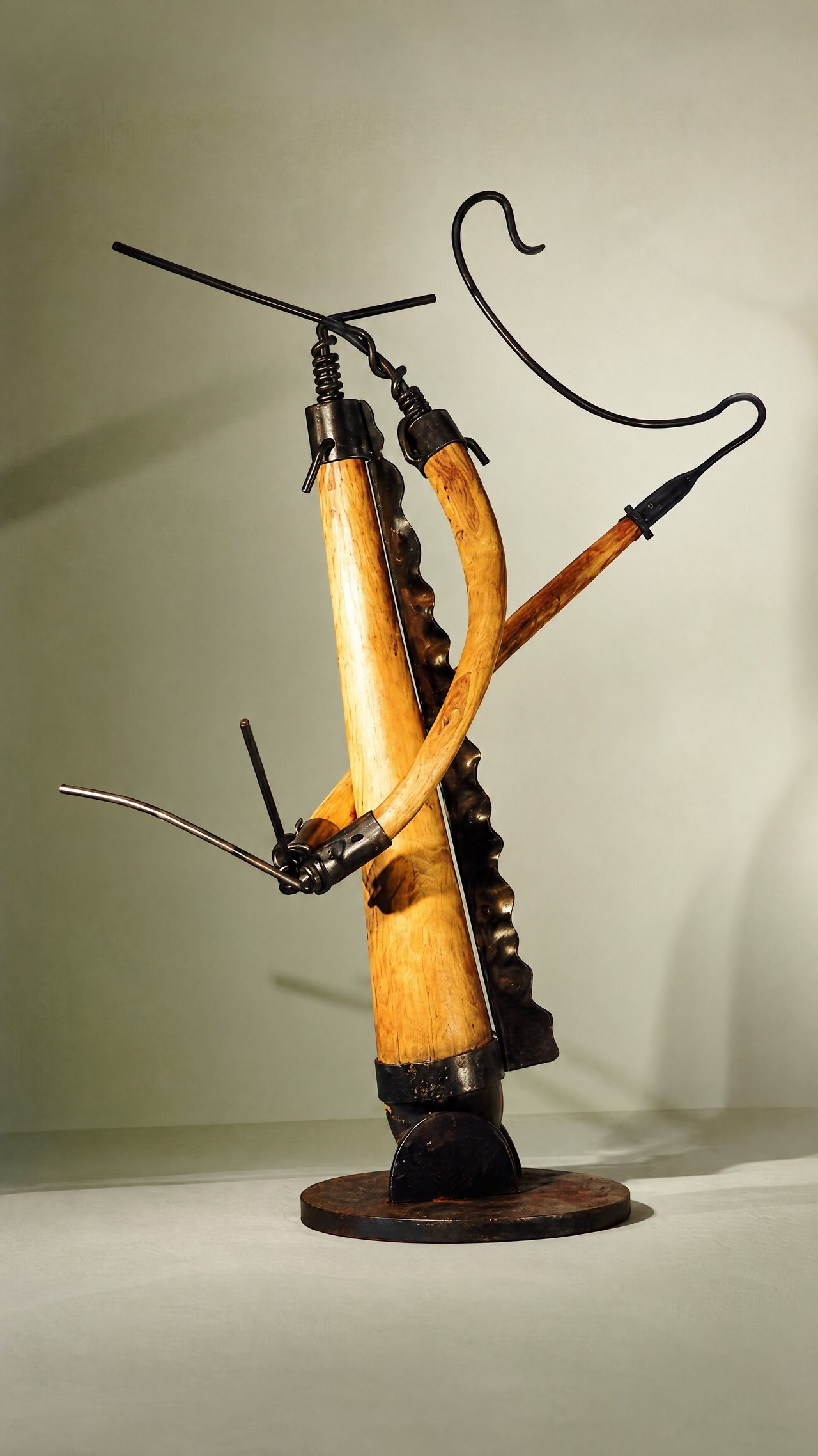 Sting, two curved wooden horns ribbed with black steel bands, crossed and mounted on a round base with a steel hook above, by David Hamilton