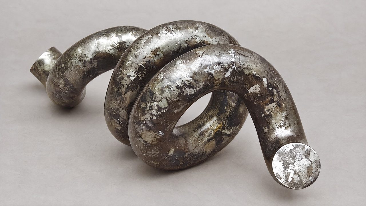 Fragment, a coiled length of silver-grey painted steel lying on its side, by David Hamilton