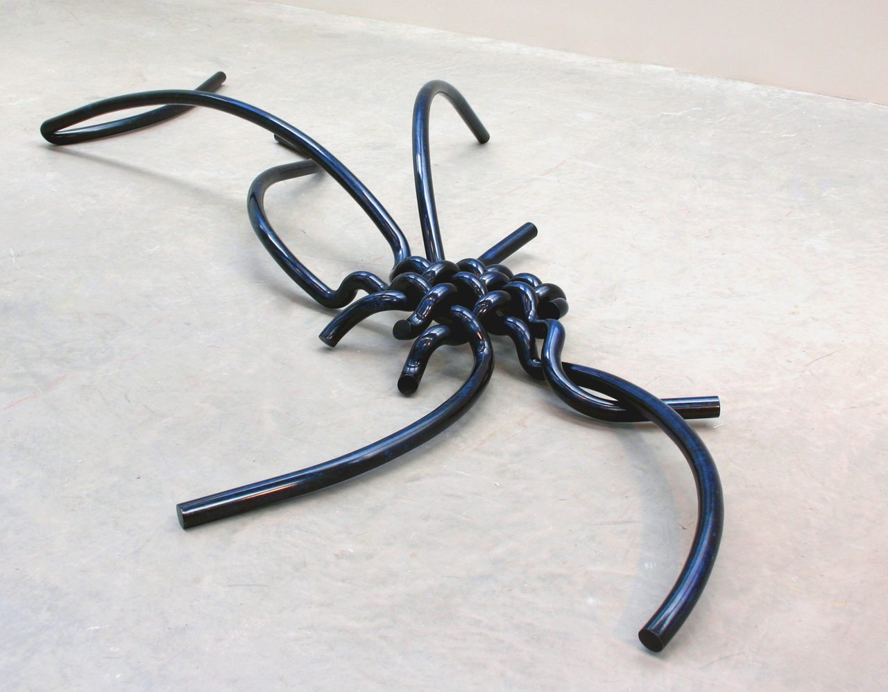 Woven, a tangle of dark blue-black painted steel rods knotted together with several loose ends splayed outward, by David Hamilton