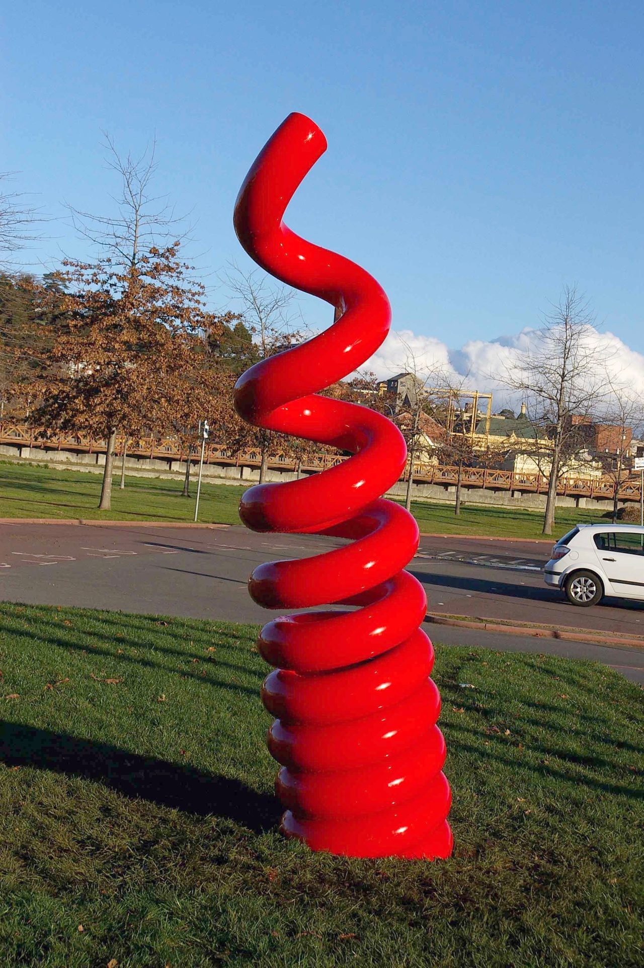 A red-orange steel wall sculpture of looping coils and sharp zigzag peaks, by David Hamilton