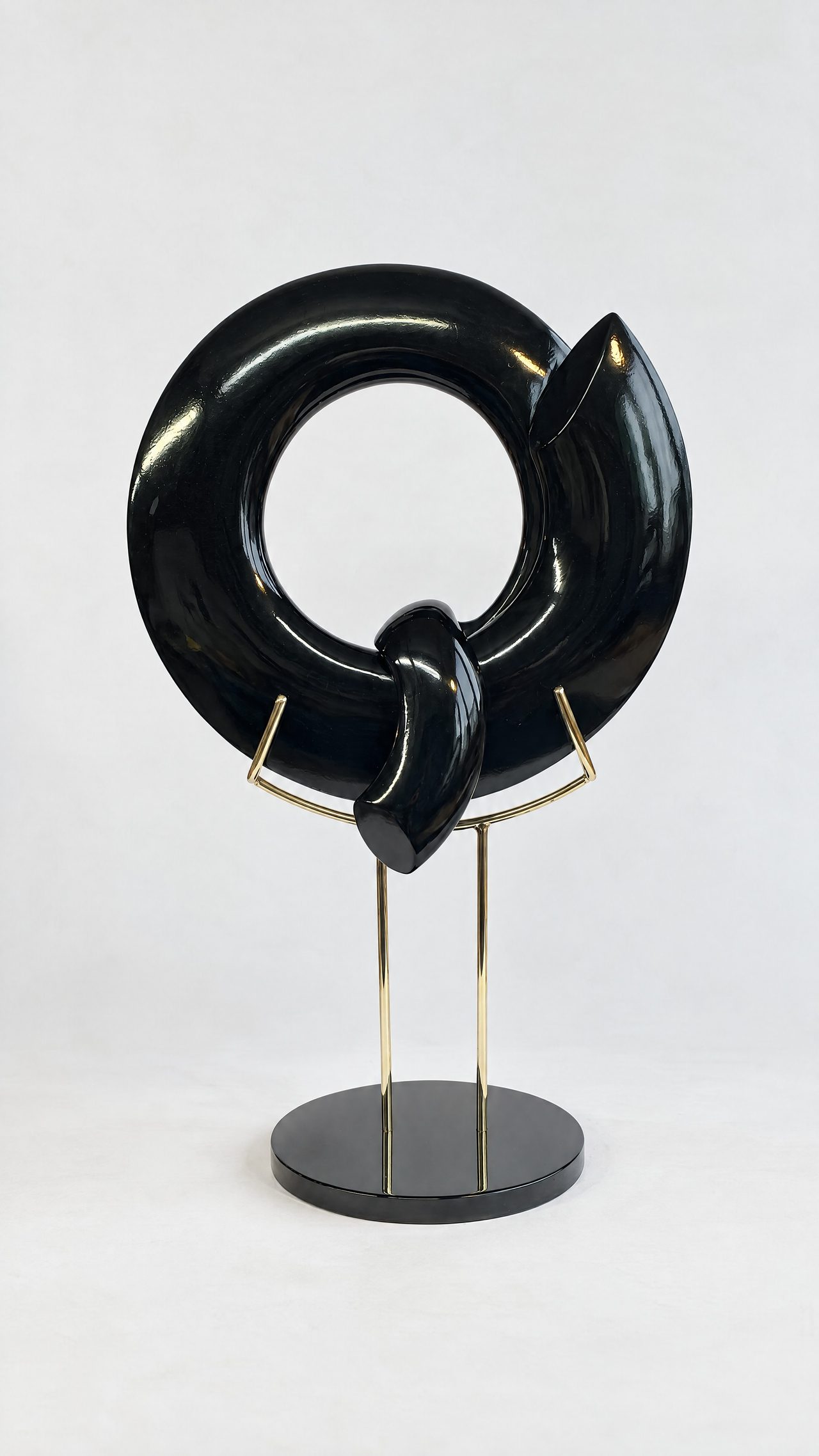 A broken-ring sculpture in glossy black lacquer with a twisted knot at its base, mounted on a stand, by David Hamilton